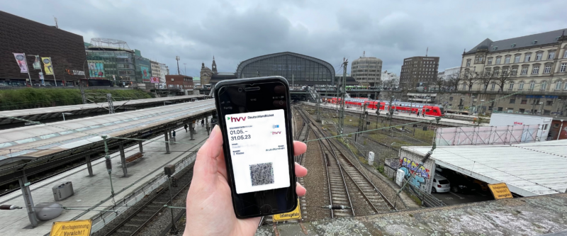 Foto des Deutschlandtickets auf dem Smartphone, im Hintergrund der Hamburger Hauptbahnhof