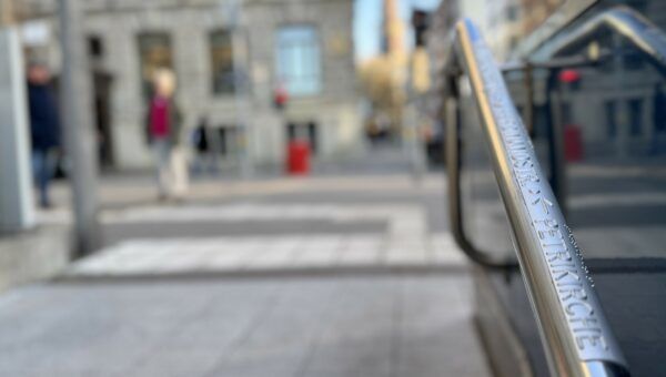 Foto eines Handlaufs am Jungfernstieg, der mit einer Plakette ausgestattet ist: In Braillie- und Klarschrift weist sie den Weg zur Petrikirche.