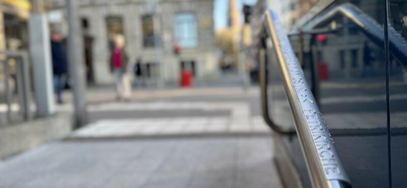 Foto eines Handlaufs am Jungfernstieg, der mit einer Plakette ausgestattet ist: In Braillie- und Klarschrift weist sie den Weg zur Petrikirche.